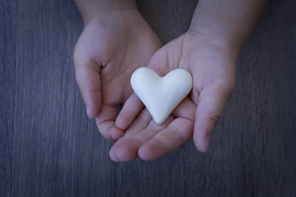 The child is holding a close-up heart. Hands on a wooden background.