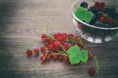 bir kase ahşap eski arka plan üzerinde kırmızı ve siyah frenk üzümü. Vintage