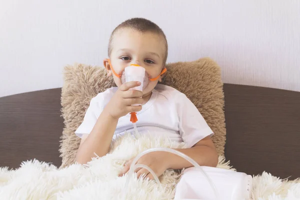 A child inhales a nebulizer at home on the bed