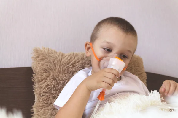 A child inhales a nebulizer at home on the bed