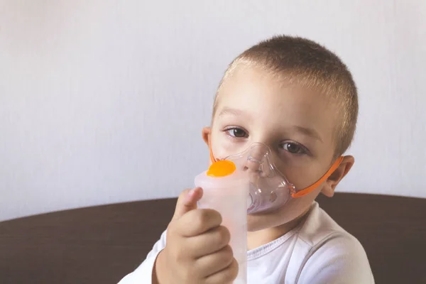 A child inhales a nebulizer at home on the bed