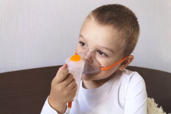 A child inhales a nebulizer at home on the bed