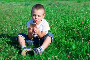 Bir çocuk çimde oturma ve hareket eden telefon içinde oynarken.