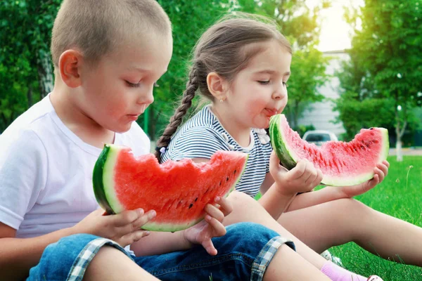 男の子と女の子の子供の夏の芝生の上に座っているとジューシーなスイカを食べる — ストック写真