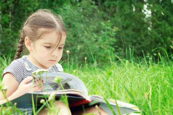 夏の少女は草の上に座っているし 屋外本を読みます ストック写真