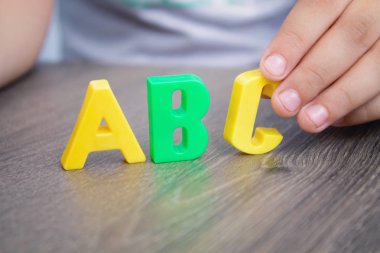 Çocuğun elinde renkli plastik harfler. Çocuk kelimeleri alfabe ekler.