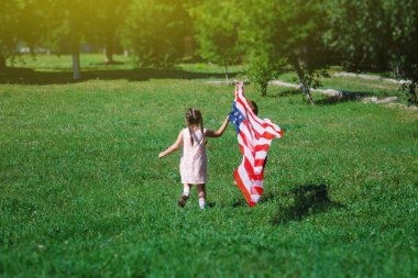 Çocuklar - bir erkek ve bir kız ile bir Amerikan bayrağı ellerinde yeşil çimenlerin üzerinde çalışan geliştirme