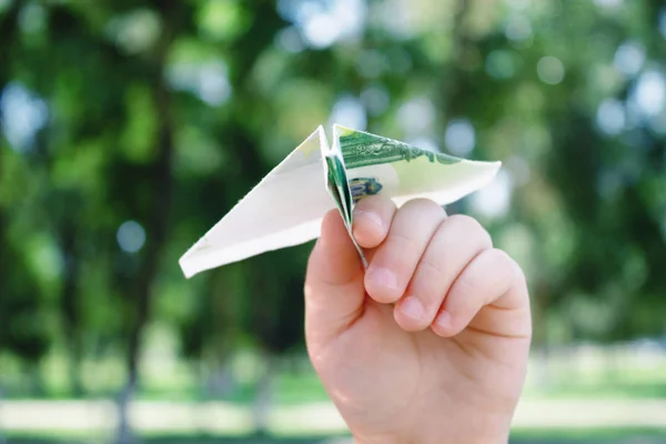 A paper airplane made from a banknote of 100 euros, in the hands of a child against the background of nature