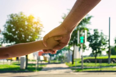 Bir çocuk için bir emniyet konsepti. Baba yaya geçidi çocuğun elini tutar. Arka planda, bulanık bir trafik işareti