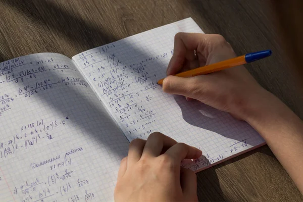 Une main féminine écrit des formules mathématiques dans un cahier. Devoirs scolaires en mathématiques — Photo