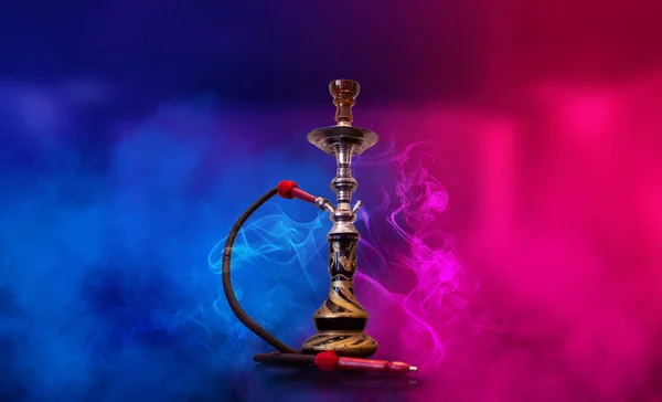 Smoking hookah on the background of an empty room. Multicolored neon light. Searchlight, laser blue and pink rays, smoke. — Stock Photo, Image