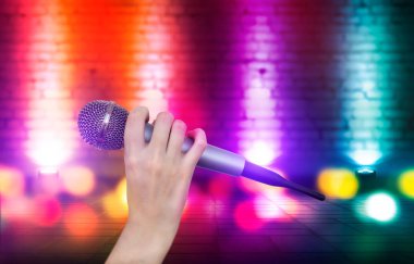 Bir kadın el Karaoke kulüp sahnesinin renkli ışıklar karşı bir mikrofon tutuyor. Bulanık Neon Işıklar ile parlak renkli arka plan