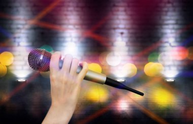 Bir kadın el Karaoke kulüp sahnesinin renkli ışıklar karşı bir mikrofon tutuyor. Bulanık Neon Işıklar ile parlak renkli arka plan