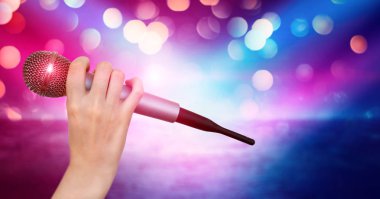 Bir kadın el Karaoke kulüp sahnesinin renkli ışıklar karşı bir mikrofon tutuyor. Bulanık Neon Işıklar ile parlak renkli arka plan