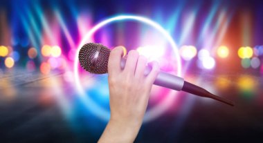 Bir kadın el Karaoke kulüp sahnesinin renkli ışıklar karşı bir mikrofon tutuyor. Bulanık Neon Işıklar ile parlak renkli arka plan