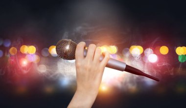 Bir kadın el Karaoke kulüp sahnesinin renkli ışıklar karşı bir mikrofon tutuyor. Bulanık Neon Işıklar ile parlak renkli arka plan