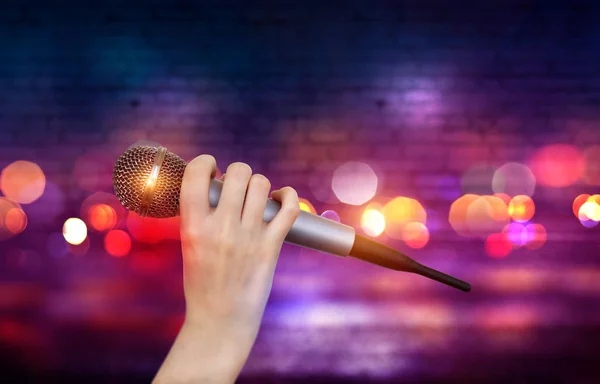 Bir kadın el Karaoke kulüp sahnesinin renkli ışıklar karşı bir mikrofon tutuyor. Bulanık Neon Işıklar ile parlak renkli arka plan