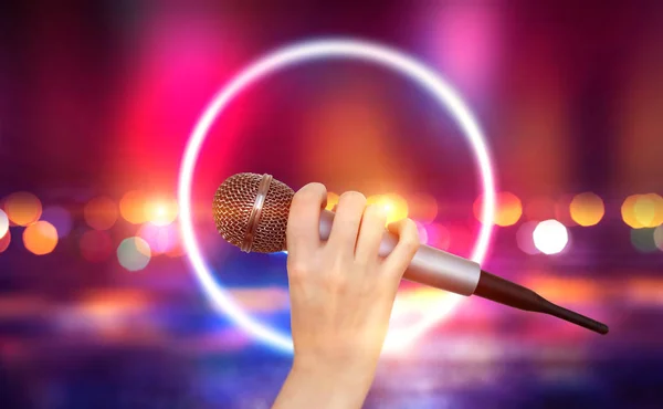 Samice drží jeden mikrofon proti barevným světlicím scény v karaoke klubu. Světlé barevné pozadí se rozmazanou neonové světlíky — Stock fotografie
