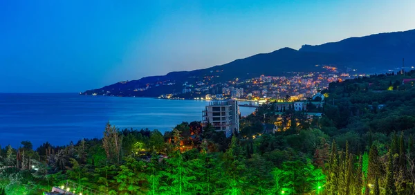 View of the evening city by the sea, illuminated by lights. The city of Yalta after sunset.
