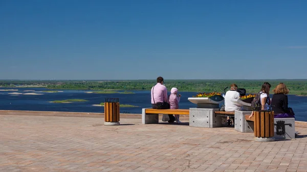 Several people sit on benches on a Sunny summer day. It offers views of the nearby river and vast expanses.