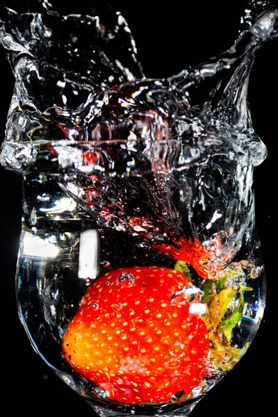 Stänk ande vatten i glas bägare från fallna jordgubbar — Stockfoto
