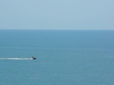 Parasailing. Tekne denizde, onu paraşütle takip eden bir adam takip ediyor. Deniz kenarında aktif tatiller. Güneşli bir yaz gününde.