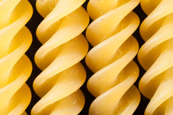 Spiral pasta from durum wheat in a row on a dark background, clo — Stock Photo, Image