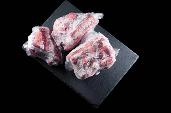 Zmrazené maso v plastikové tašce na kamenné stojce na černém backgro — Stock fotografie