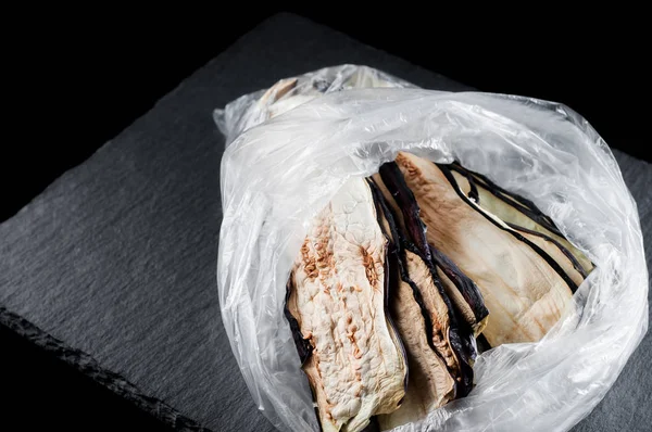 Bevroren gedroogde aubergine in een plastic zak op een stenen bord op een bla — Stockfoto