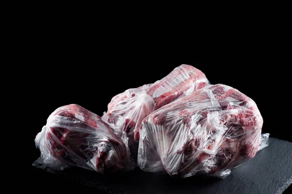 frozen meat in a plastic bag on a stone stand on a black backgro