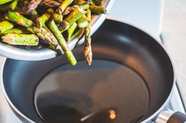 Bir kaseden tavaya doğranmış ve baharatlı kuşkonmaz dökme süreci