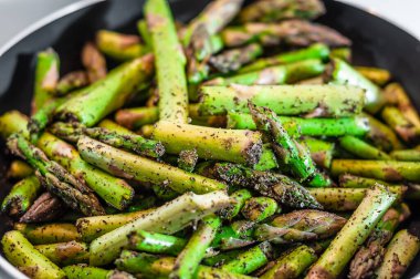 Fresh juicy asparagus sliced into pieces seasoned and salted lies in a pan