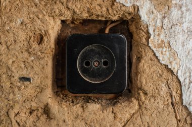 Kil bir duvara kazınmış eski siyah bir soket. Elektroniklerin duvarlardan onarılıp sökülmesi