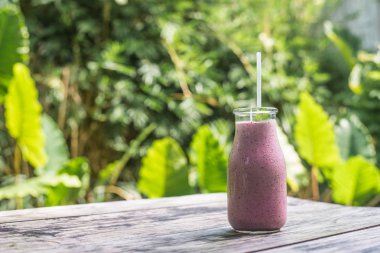 smoothies ile bir plastik tüp, bir kafe Endonezya, Bali Adası tropik yeşil zemin üzerine eski ahşap masa üzerinde şişe