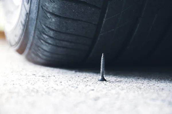 道路上の鋭い金属ネジの近くに車のタイヤを穿刺する — ストック写真