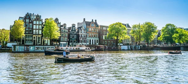 7 Mayıs 2018 - Amsterdam, görüntülemek bir yaz gününde küçük tekne ve içinde belgili tanımlık geçmiş geleneksel evleri Amstel dolu Nehri üzerinde