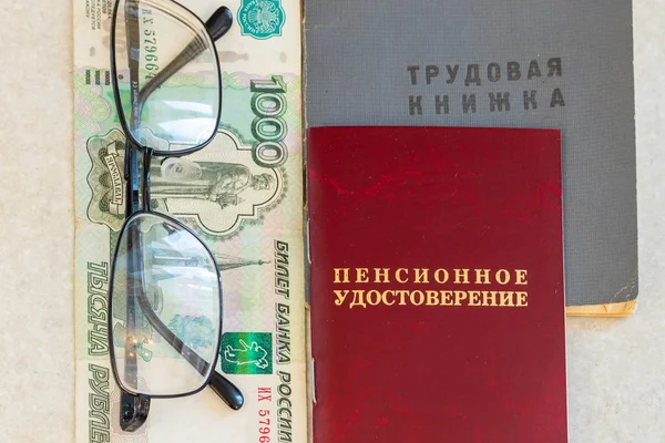 Employment history of the employee, a pension certificate, glasses and money are on the table. Inscriptions on the certificate: \'work book\' and \'Pension certificate\'