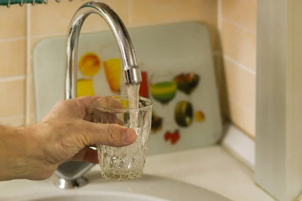 a man's hand pours water into a glass under the tap in the kitchen