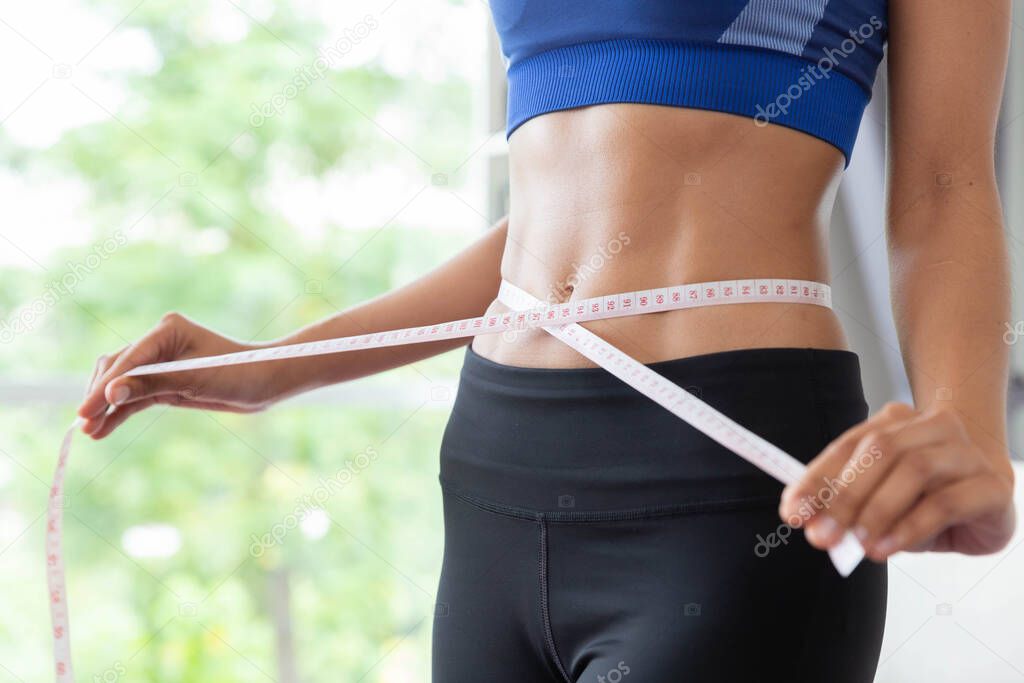 Slim young asian woman measuring herself with measureing tape at home