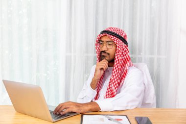 Arap işadamı ofisinde bilgisayar defteri ve cep telefonuyla işine odaklanıyor