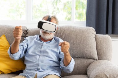 Emekli kıdemli bir adam evindeki oturma odasında VR cihazıyla oynuyor.