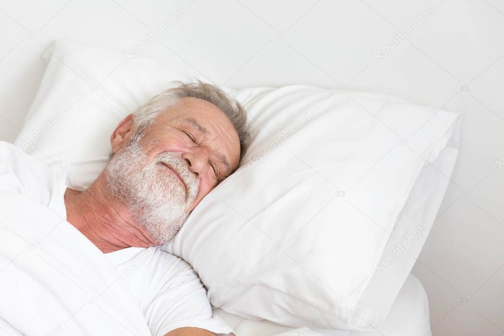 Senior retirement man sleeping happily in his white blanket bed in bedroom