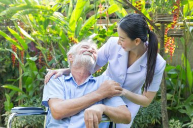Bir hemşire, evdeki bahçesinde tekerlekli sandalyedeki yaşlı bir erkeğe bakıyor.