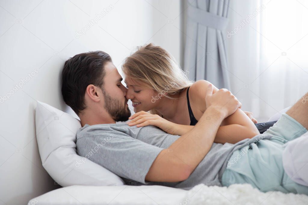 Caucasion couple kiss on bed in bedroom