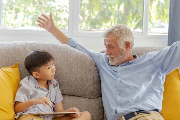 爷爷和小可爱的孙子在家里沙发上一起玩触摸屏平板电脑 — 图库照片