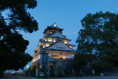 Osaka Kalesi 'nin ana kulesinin gece görüşü yamaçta ağaçlarla aydınlandı.