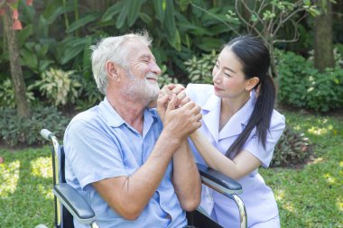 Bir hemşire, evdeki bahçesinde tekerlekli sandalyedeki yaşlı bir erkeğe bakıyor.