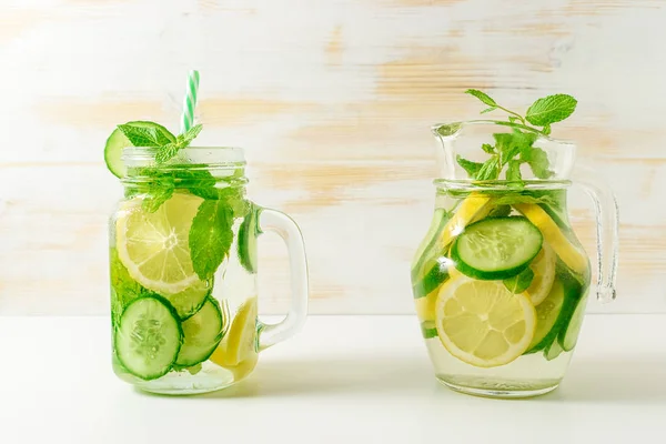 Detox water infused with sliced lemon, cucumber and sprigs of mint on wooden background.