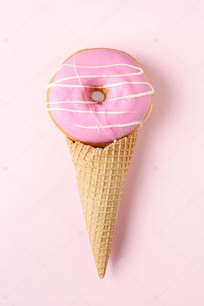 Pink glazed donut with ice cream cone on pink pastel background. Flat lay. Creative concept.