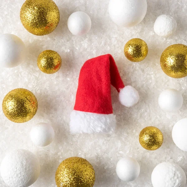 Gold and white glitter ball decorations with Santa Claus hat in the snow. Christmas or New Year holiday background.